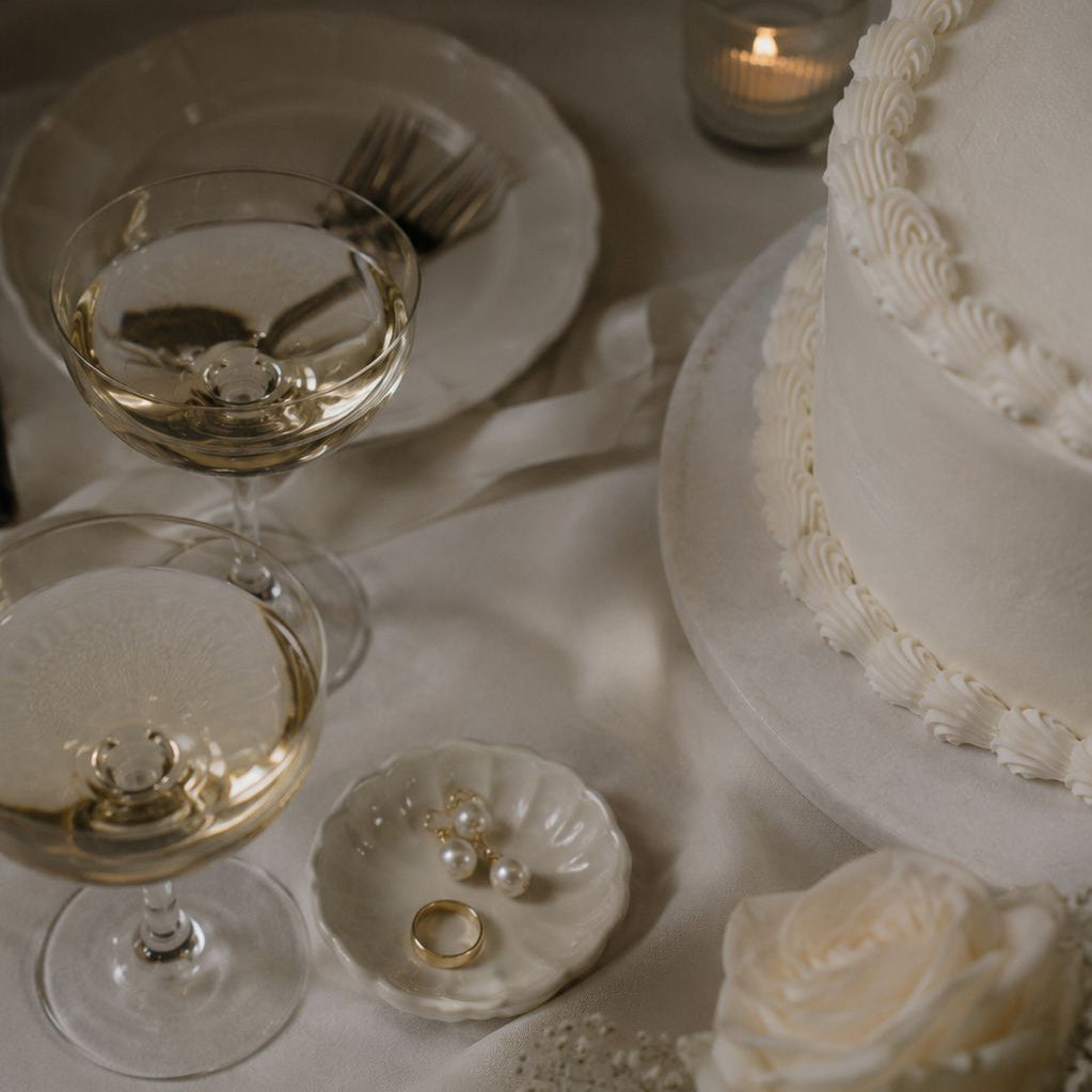Stijlvol gedekte tafel met champagne glazen, wit porselein servies, een bruidstaart en witte rozen