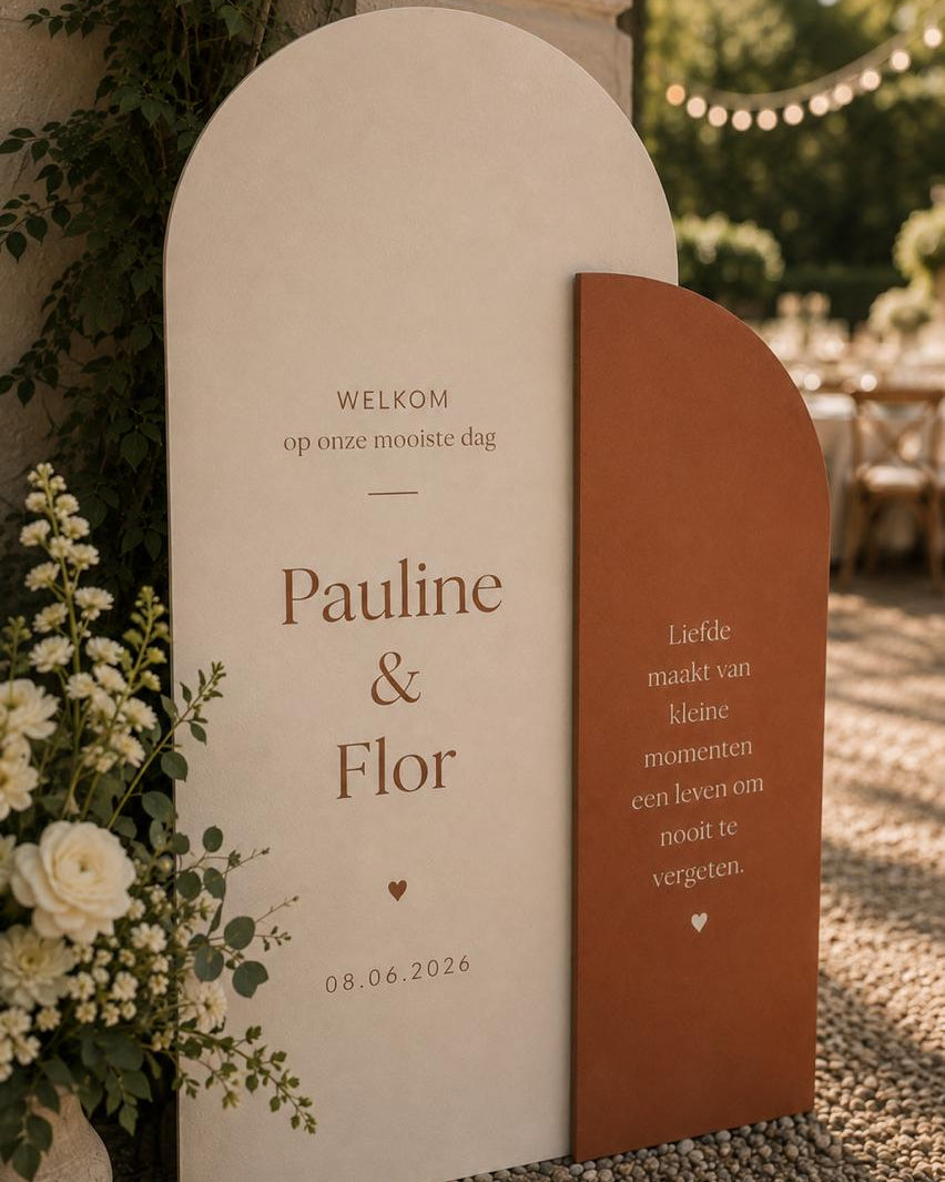 Twee houten bogen met welkomsttekst en bloemwerk bij de ingang van een trouwlocatie