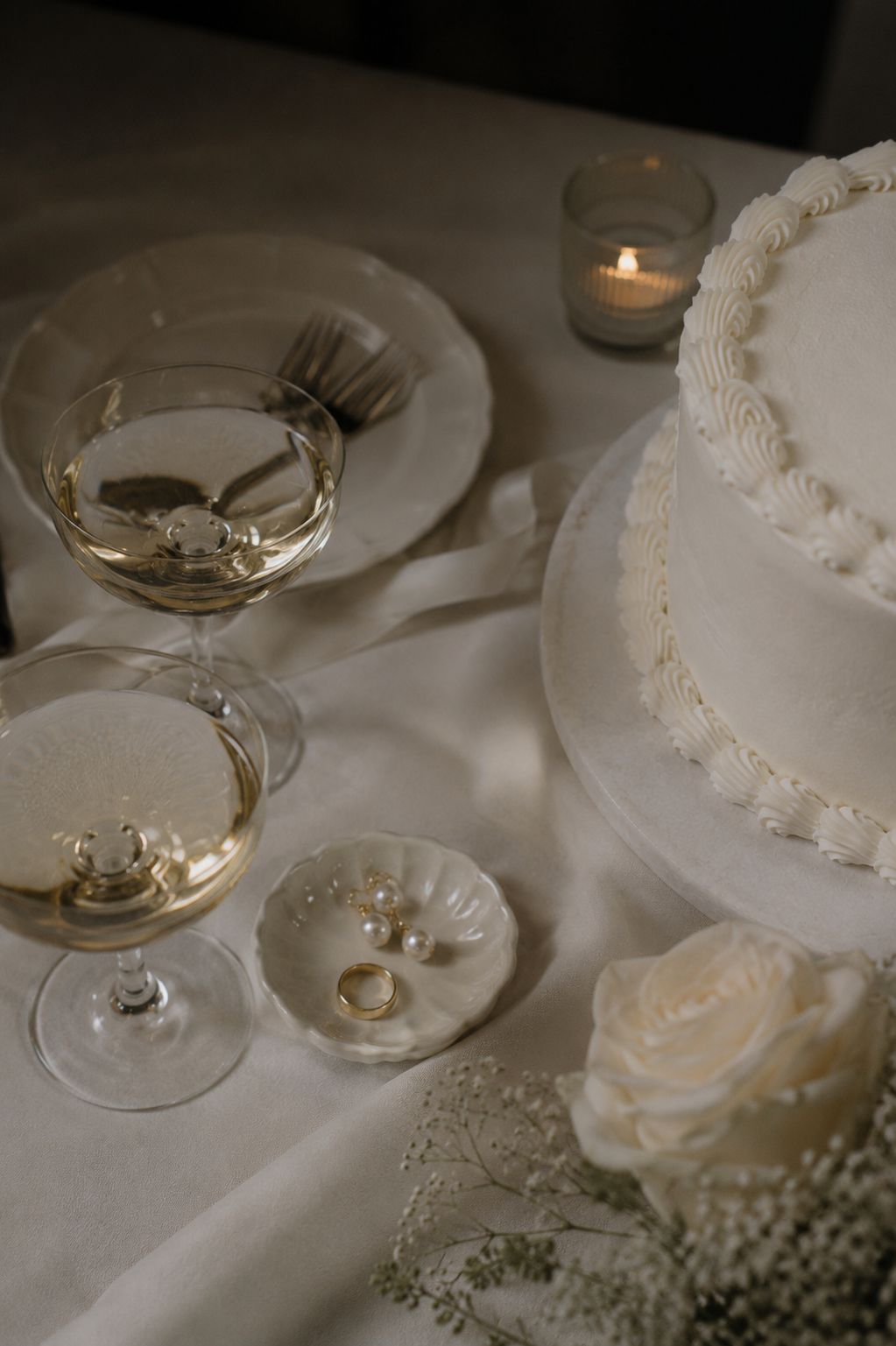 Stijlvol gedekte tafel met champagne glazen, wit porselein servies, een bruidstaart en witte rozen